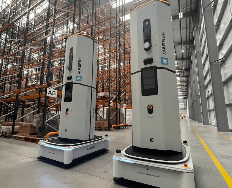 Two Dexory autonomous robots deployed in a Maersk warehouse, scanning tall pallet racking