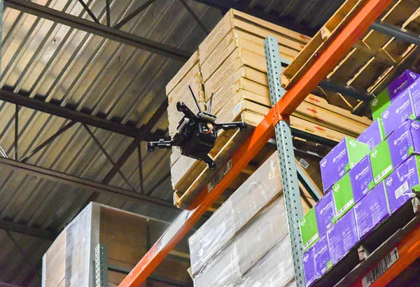 Autonomous warehouse inventory drone scanning a high-bay pallet rack in an active facility